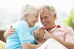 Senior Couple Sitting On Outdoor Seat Together Laughing